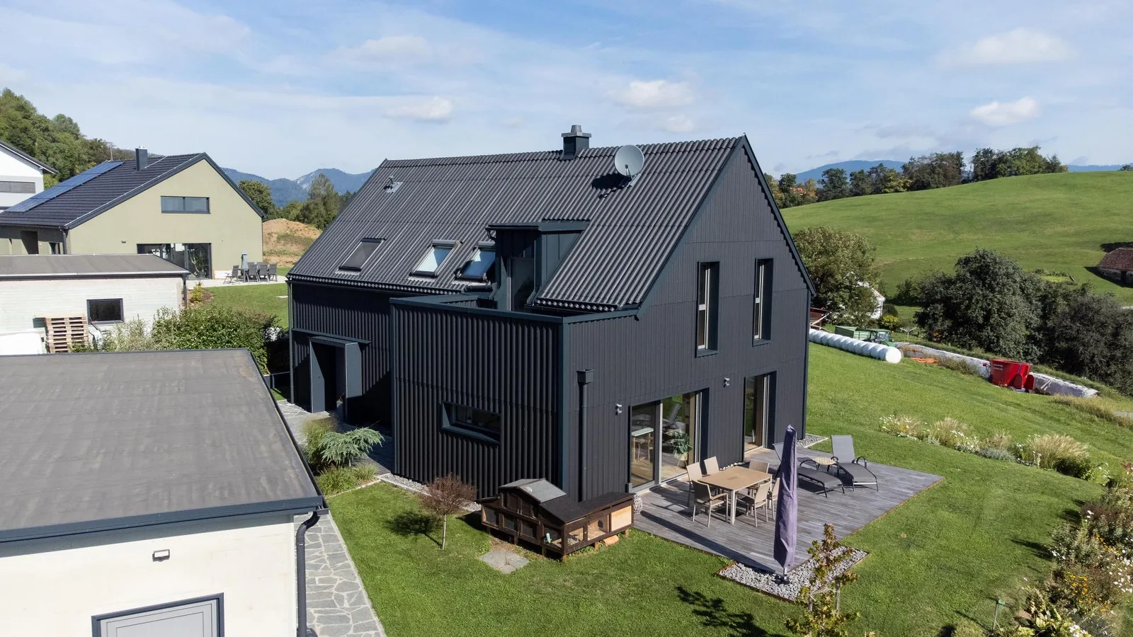 Dunkles Wohnhaus mit gewelltem Dach und gewellter Fassade, davor eine Terrasse