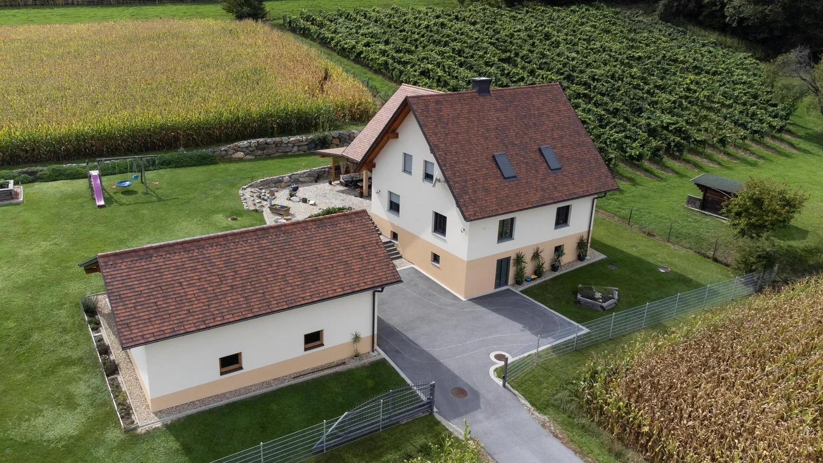 Wohnhaus und Nebengebäude mit rotbraunem Ziegeldach vor einem Weinberg