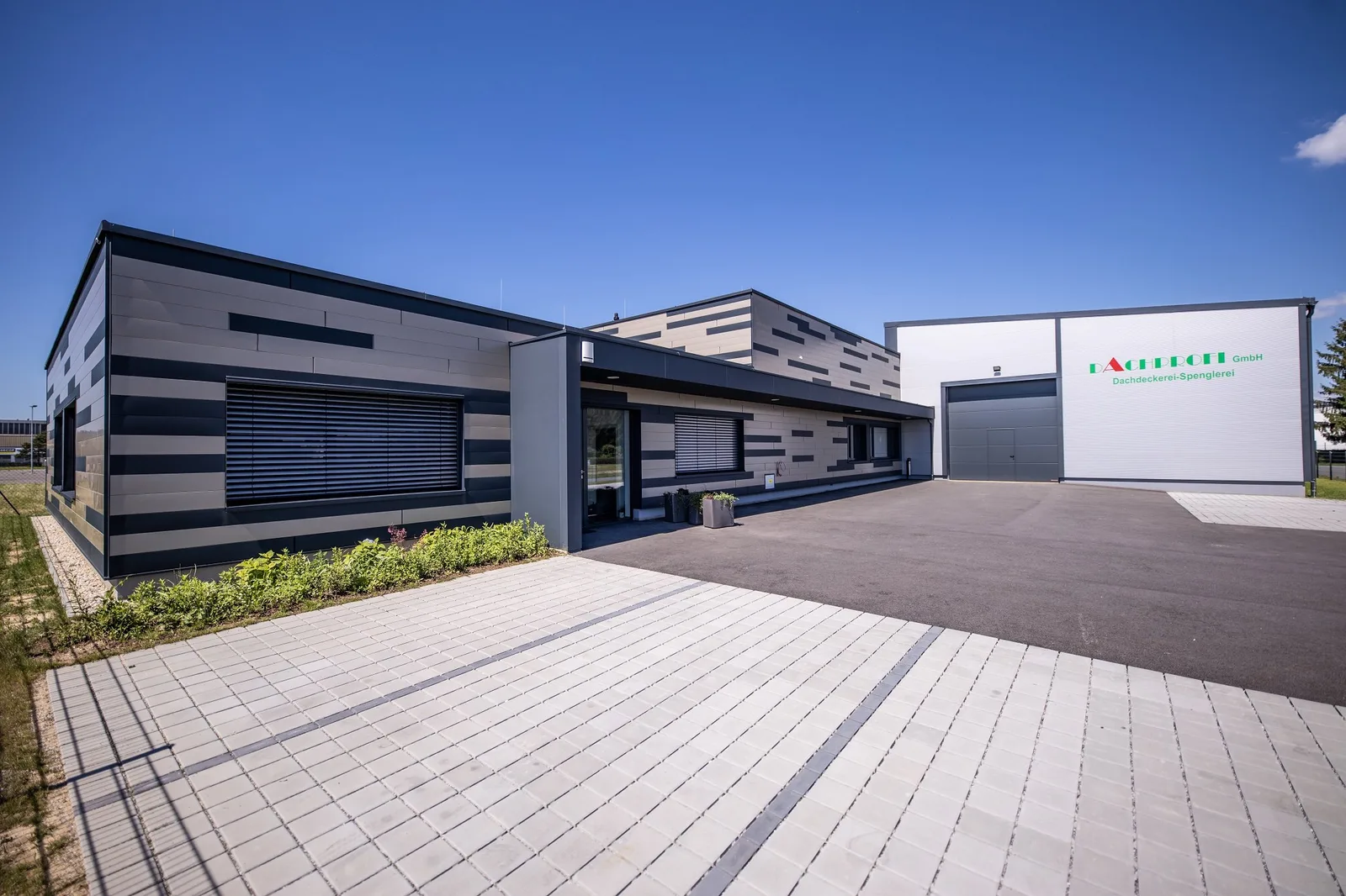 Firmengebäude mit Schriftzug Dachprofi GmbH Dachdeckerei-Spenglerei unter blauem Himmel